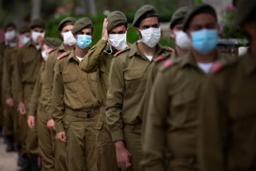 Israeli soldiers wearing protective face masks amid concerns over the country's coronavirus outbreak, stand next to graves of fallen soldiers on the eve of memorial Day in Kiryat Shaul Military Cemetery in Tel Aviv, Israel, Monday, April 27, 2020. This year the government had banned public memorial services at military cemeteries as part of its measures to help stop the spread of the virus. Israel marks the annual Memorial Day in remembrance of soldiers who died in the nation's conflicts, beginning at dusk Monday until Tuesday evening. (AP Photo/Oded Balilty)