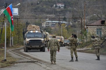 Azerbaijani soldiers film Azeri military trucks moving through the town of Lachin on December 1, 2020. - Azerbaijani soldiers and military trucks on December 1 rolled into the final district given up by Armenia in a peace deal that ended weeks of fighting over the disputed Nagorno-Karabakh region. (Photo by Karen MINASYAN / AFP)